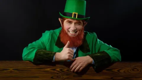 Muškarac kostimiran u vilenjaka s visokim zelenim šeširom i crvenom bradom.