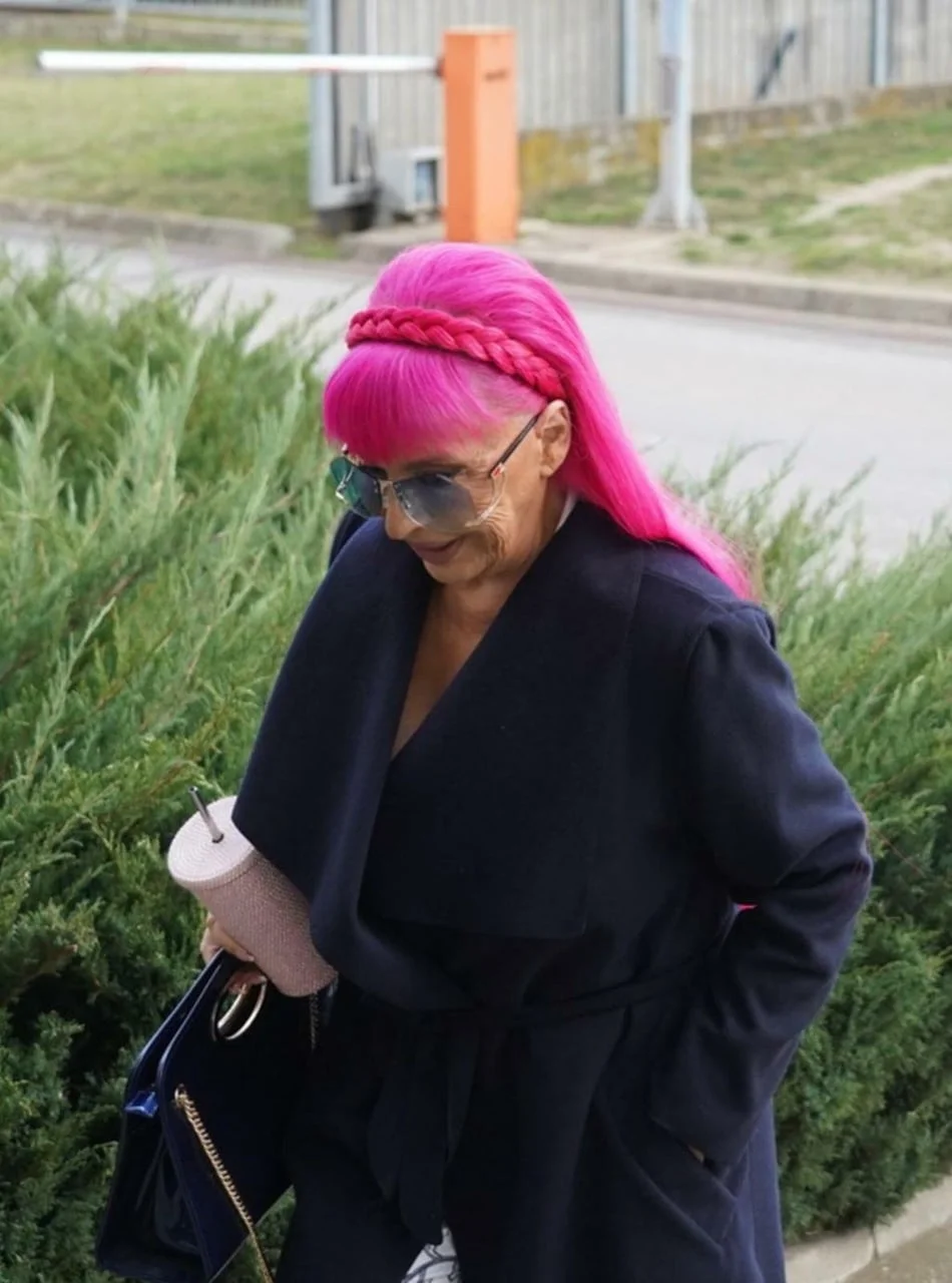 Zorica Brunclik u tamnom kaputu hoda stazom pored zelenog grmlja.