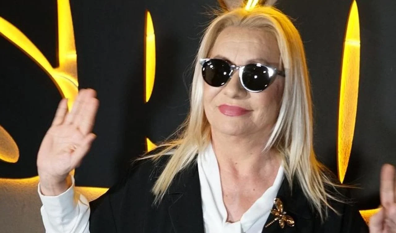 Plavokosa žena sa sunčanim naočalama i zlatnim brošem u obliku vilin konjica.