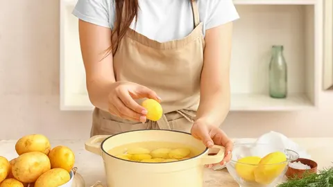 Žena u kuhinji polagano stavlja oguljeni krumpir u lonac s vodom
