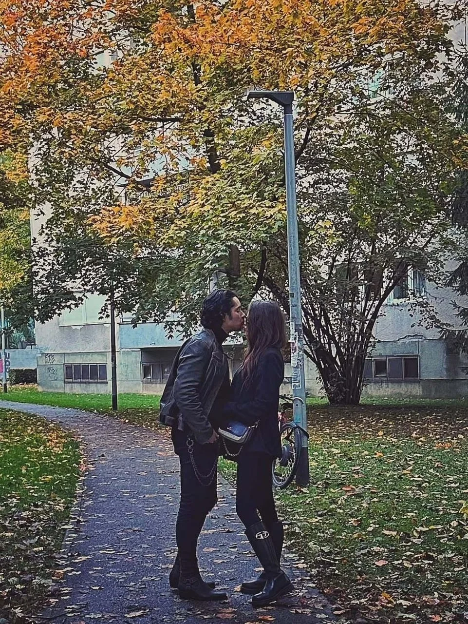 Par se ljubi na pješačkoj stazi u parku okružen jesenskim lišćem i drvećem.