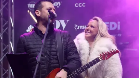 Damir Ridjan pjeva na pozornici uz plavokosu ženu tijekom nastupa.