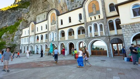 Bijela zgrada manastira urezana u strmi stjenjak s posjetiteljima