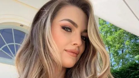 Portret mlade žene s plavim pramenovima i blagim osmijehom na otvorenom.