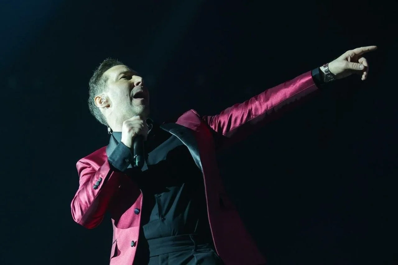 Glazbenik na koncertu s mikrofonom u ruci pod scenskim svjetlima.