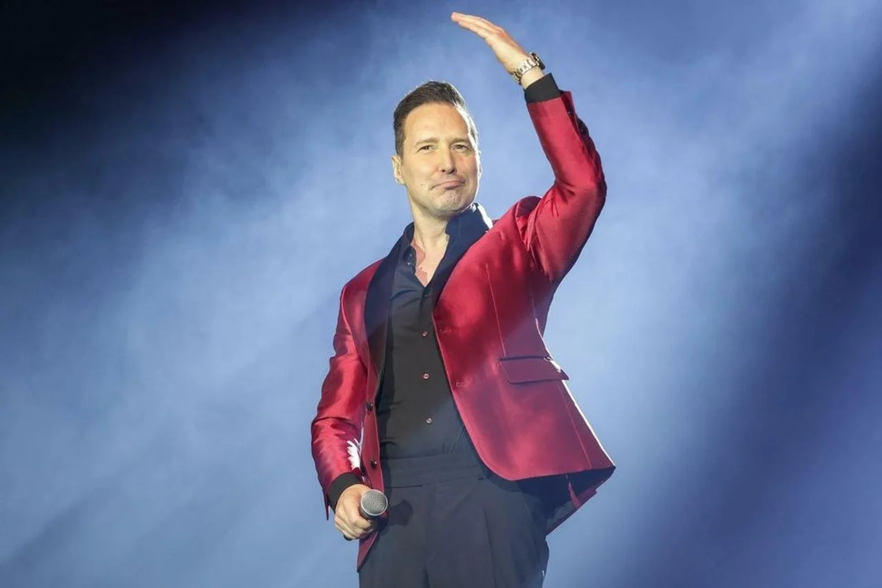 Peđa Jovanović u crvenom sakou pozdravlja publiku s podignutom rukom.