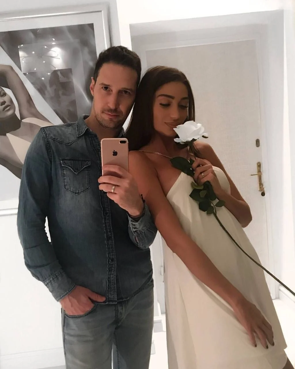 Muškarac i žena snimaju selfie u ogledalu, ona drži bijelu ružu.