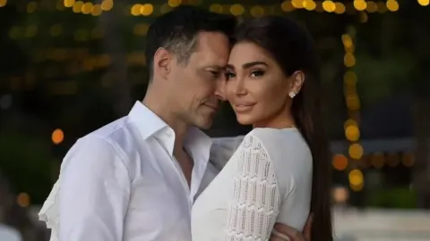 Peđa Jovanović i njegova supruga poziraju zagrljeni u bijeloj odjeći.