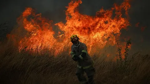 Vatrogasac u zaštitnoj opremi stoji ispred velikog požara u travi