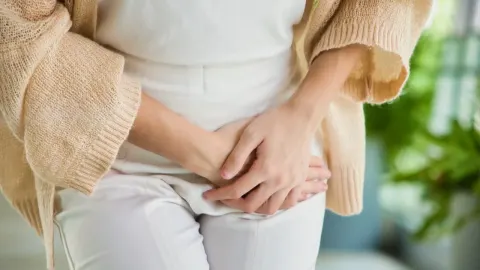 Žena drži ruke na donjem dijelu trbuha izražavajući bol ili nelagodu u mjehuru.