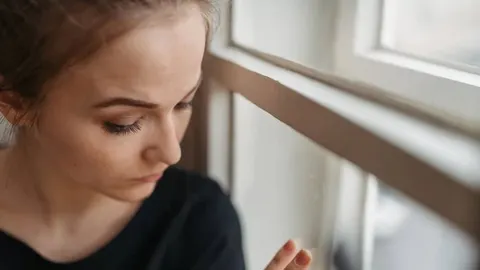 Zabrinuta mlada žena gleda kroz prozor s tužnim izrazom lica