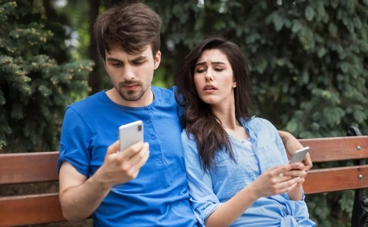 Muškarac i žena na klupi koji sumnjičavo gledaju u mobilni telefon