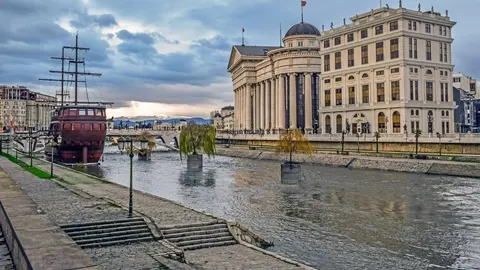Pogled na rijeku Vardar, drveni brod i neo-klasičnu arhitekturu u Skoplju