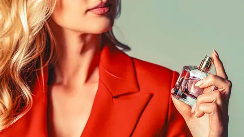 Žena u crvenom sakou drži staklenu bočicu parfuma