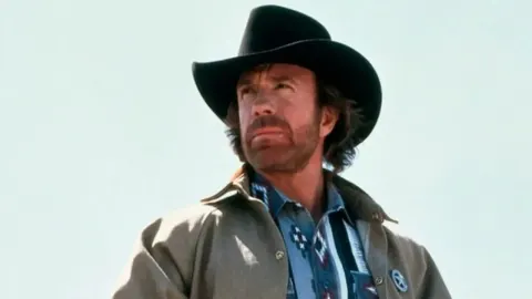 Chuck Norris s crnim kaubojskim šeširom i bradom gleda u daljinu