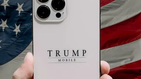 Bijeli pametni telefon s natpisom Trump Mobile ispred američke zastave
