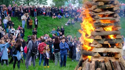 Velika vatra od drva na zelenom brežuljku okružena skupinom ljudi