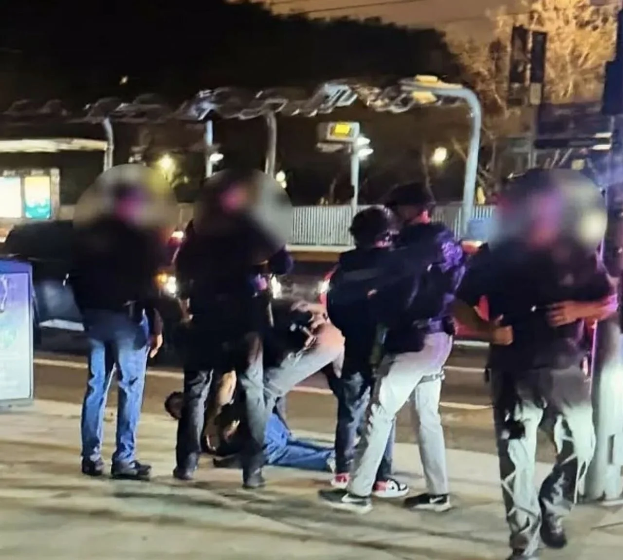 Policajci na ulici drže osobu na tlu dok su lica prisutnih zamagljena.