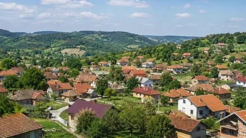 Panorama sela s kućama crvenih krovova okruženog zelenim brdima