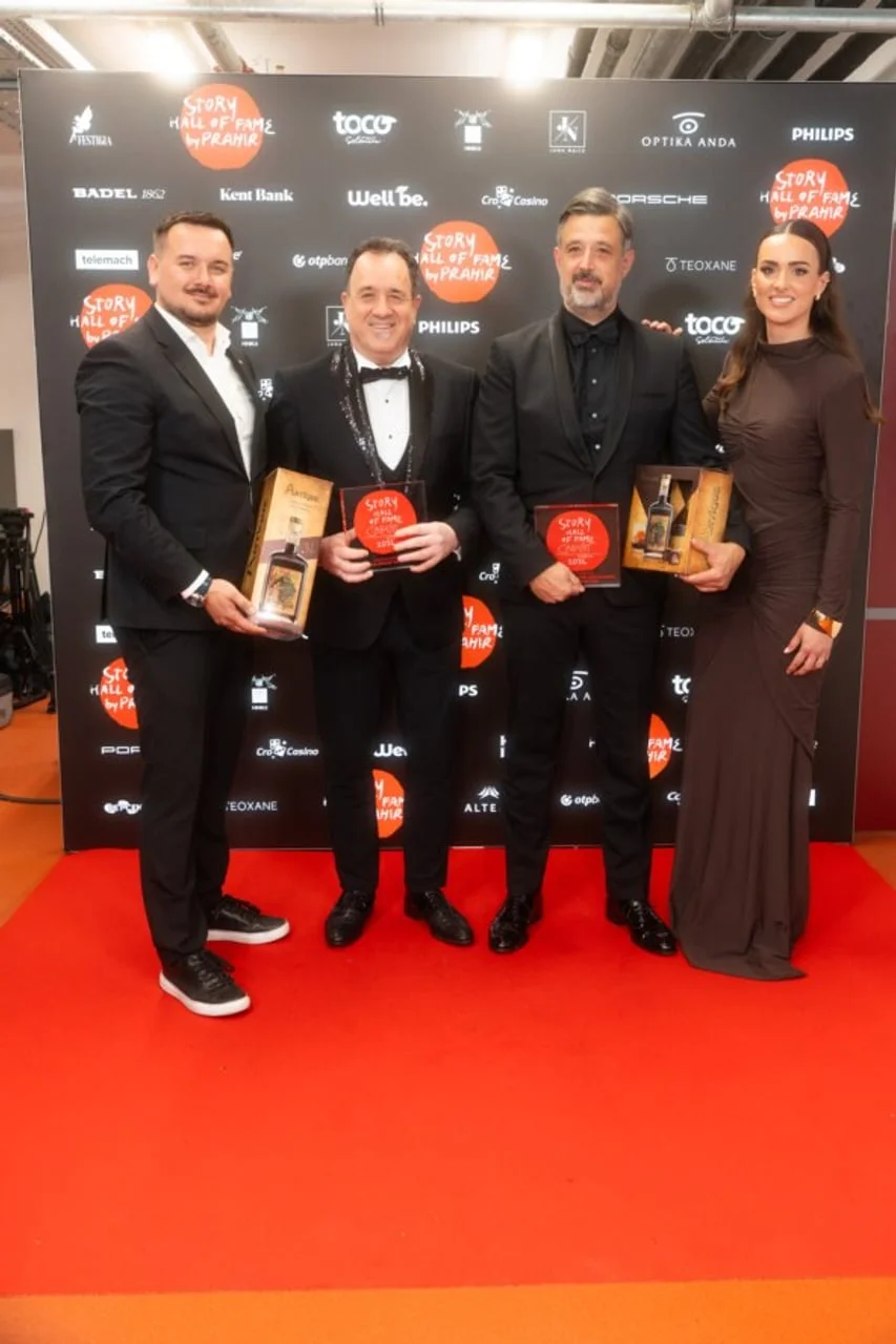 Četvero ljudi u elegantnim odjećama s nagradama ispred sponzorskog zida