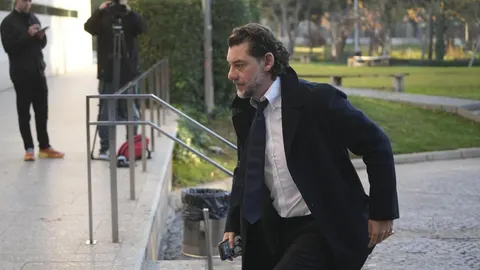 Muškarac u tamnom kaputu i bijeloj košulji hoda pored staze