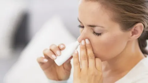 Žena koristi sprej za nos držeći jednu nosnicu zatvorenom prstima