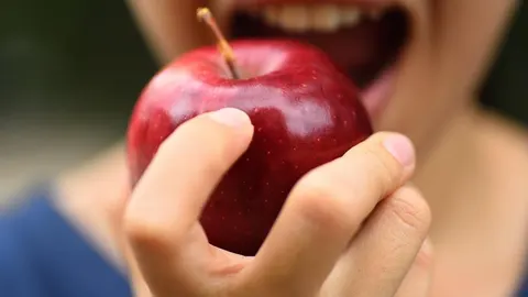 Krupni plan ruke koja drži crvenu jabuku ispred usta osobe
