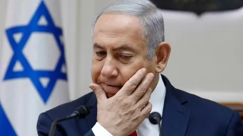 Benjamin Netanyahu s ozbiljnim izrazom lica ispred zastave Izraela
