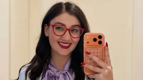 Portret nasmijane žene s crvenim naočalama i ljubičastom mašnom