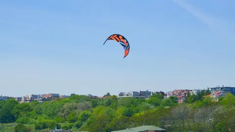 Narančasti zmaj za kite-surfing na plavom nebu iznad obalnog grada
