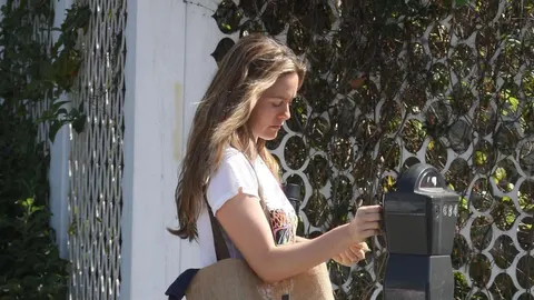 Alicia Silverstone u bijeloj majici stoji pored crnog poštanskog sandu