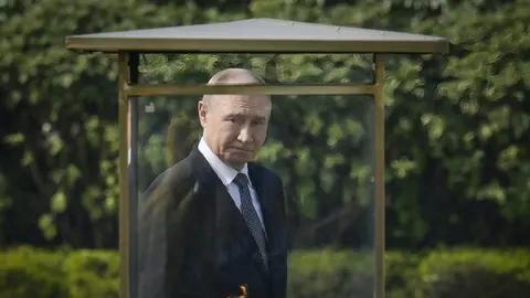 Vladimir Putin u tamnom odjełu stoji iza staklene zaštite