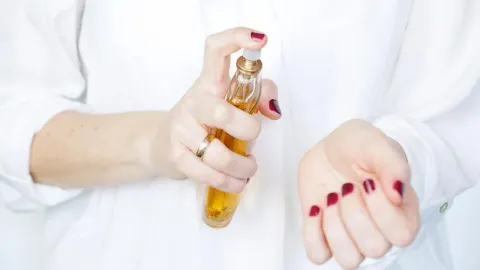 Žena nanosi parfem iz bočice na zapešće ruke