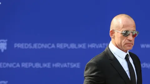 Bruce Willis u crnom odelu i sunčanim naočalama ispred plave pozadine