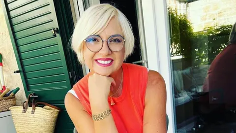Portret nasmijane plavokose žene u narančastoj majici s naočalama