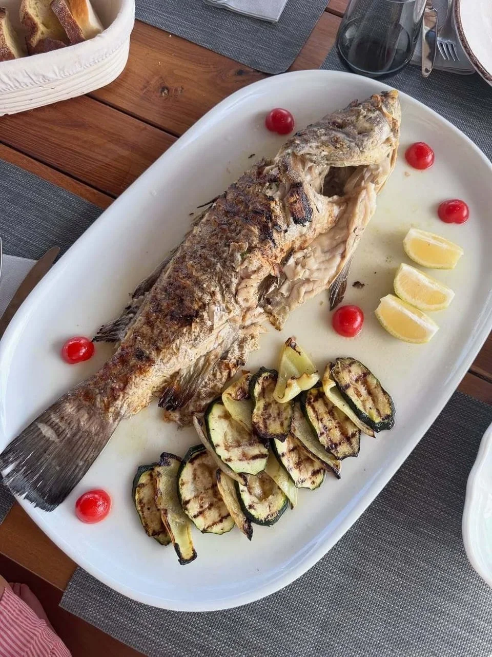 Pečena riba s grilanim tikvicama i limunom na bijelom tanjuru