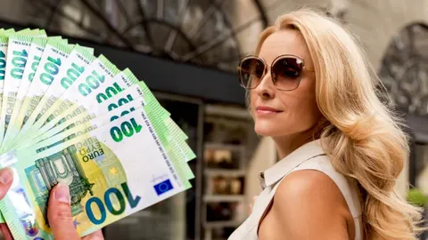 Plavuša u sunčanim naočalima drži više novčanica od 100 eura