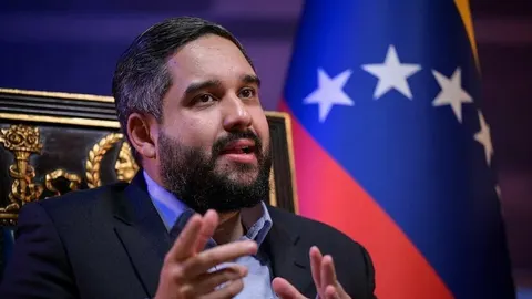 Muškarac s bradom u odelu pored zastave Venezuele