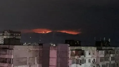 Noćni horizont s crvenim plamenovima iznad zgrada