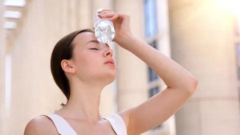 Mlada žena drži hladnu bocu vode na čelu kako bi se ohladila na suncu