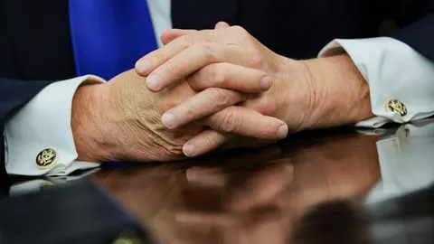 Krupni plan prepletenih ruku Donalda Trumpa na tamnom stolu