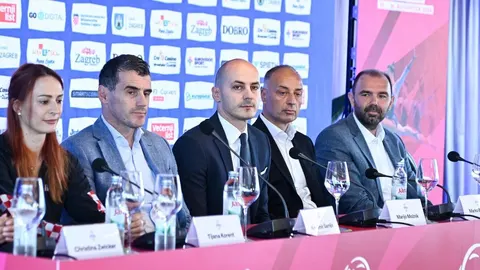 Grupa ljudi sjedi za stolom na konferenciji ispred zidnog sponzorskog panoa