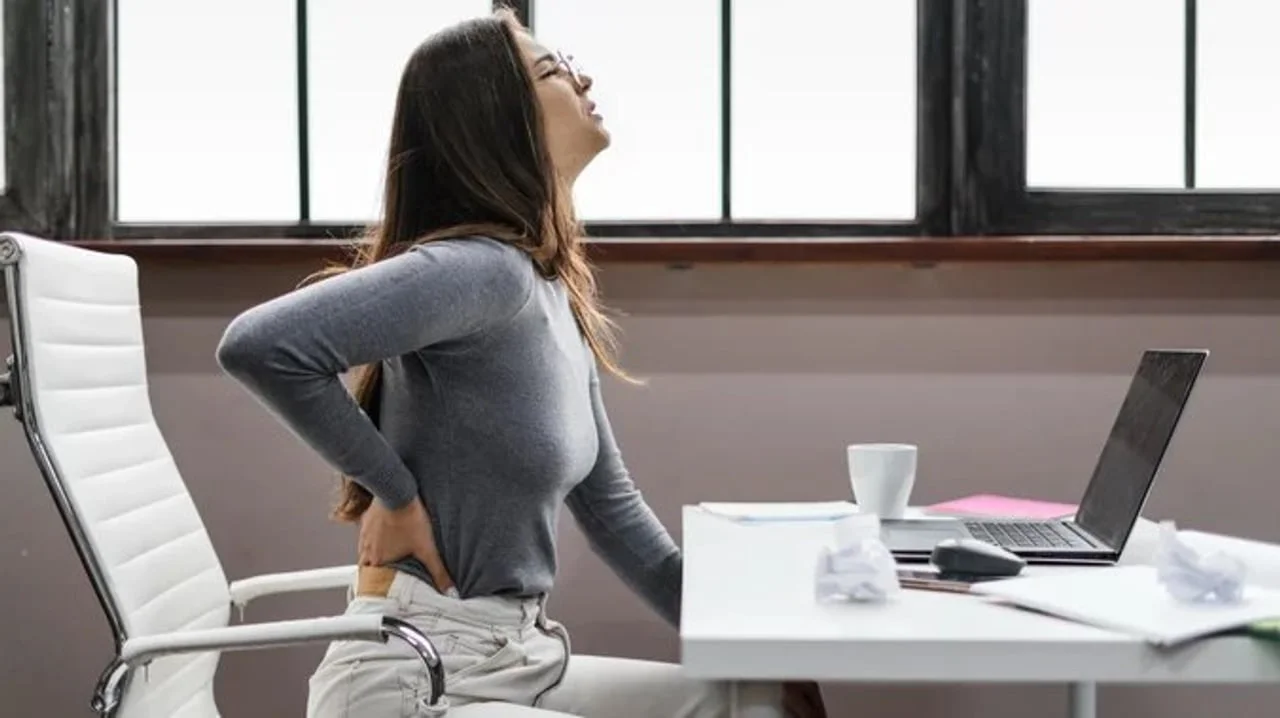 Žena s izrazom boli na licu drži leđa dok sjedi za laptopom