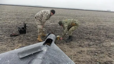 Dva vojnika u kamuflažnoj odjeći pregledavaju srušeni dron na polju
