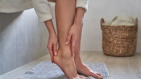 Žena u bijelom bademantilju dotiče petu svog stopala