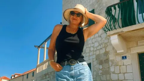 Danijela Dvornik u crnom topu, trapericama i pletenom šeširu ispred kamene kuće