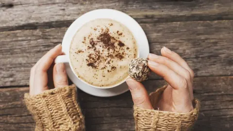 Šalica kape s pjenom i čokoladni praline u rukama osobe