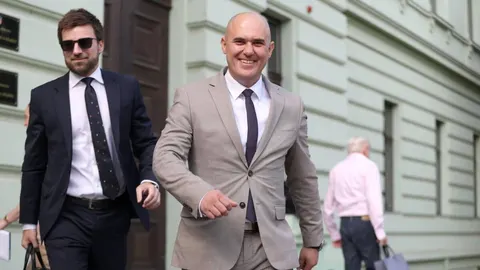 Osmijao muškarac u svijetlo smeđem odijelu i crnoj kravati