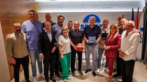 Grupa ljudi stoji u prostoriji, jedan muškarac drži košarkašku loptu