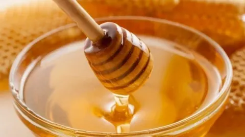 Drvena žlica za med u staklenoj zdjeli s prozirnim tečnim medom